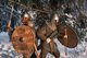 Two gladiators dressed in full armor standing back to back in a snow covered forest [Image by creator vitfedotov from AdobeStock]