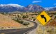 Photo of road winding through desert terrain with snow capped mountains in the background. A yellow road sign that displays an arrow that curves left. [Image by creator wakr10 from AdobeStock]