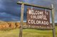 A western-style ranch sign that says "Welcome to colorful Colorado" against a dark sky and red mountains [Image by creator MarekPhotoDesign.com from AdobeStock]