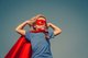 A small child in a superhero pose, wearing a blue t-shirt, red mask and red cape [Image by creator yuryimaging from AdobeStock]