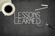 A cup of coffee, a pen, and a magnifying glass sitting on a blackboard that says "Lessons Learned" written in chalk [Image by creator Tuomas Kujansuu from AdobeStock]
